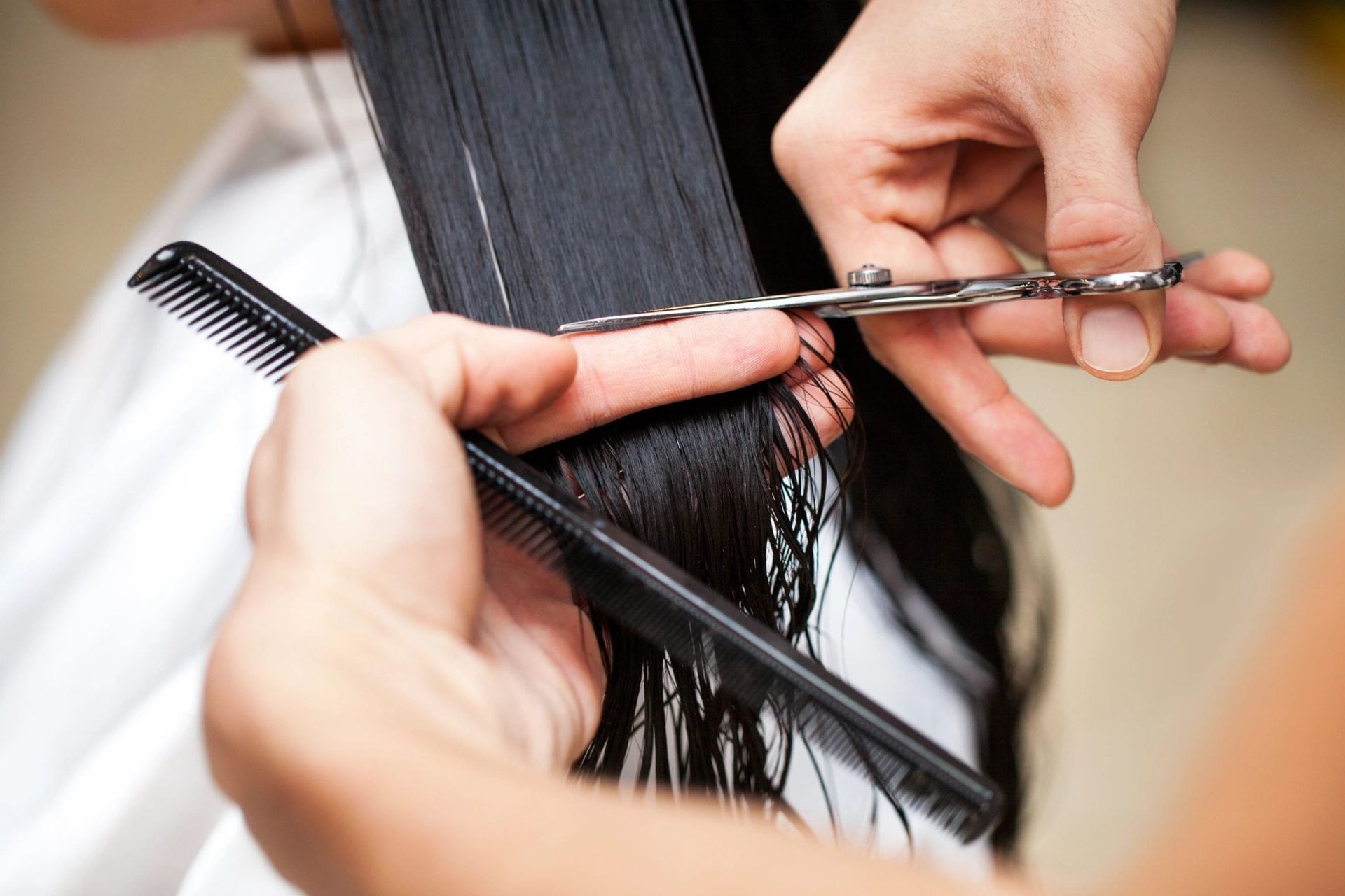A person cutting their hair with scissors and comb.